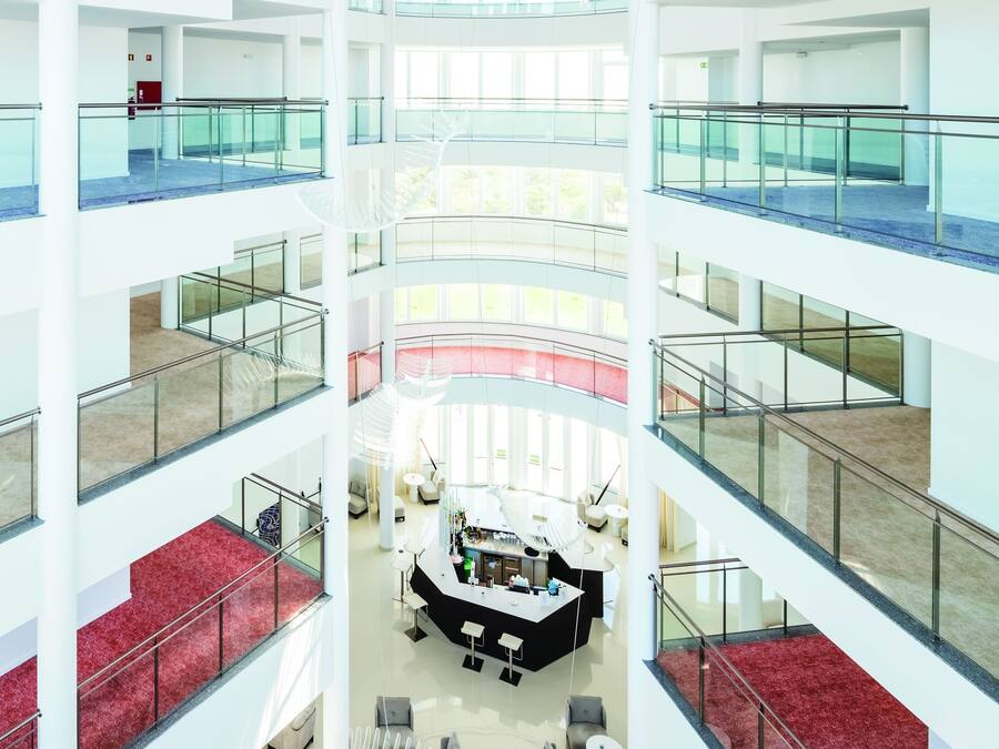 A multi-level atrium with glass railings, a central seating area, and a red carpeted staircase.