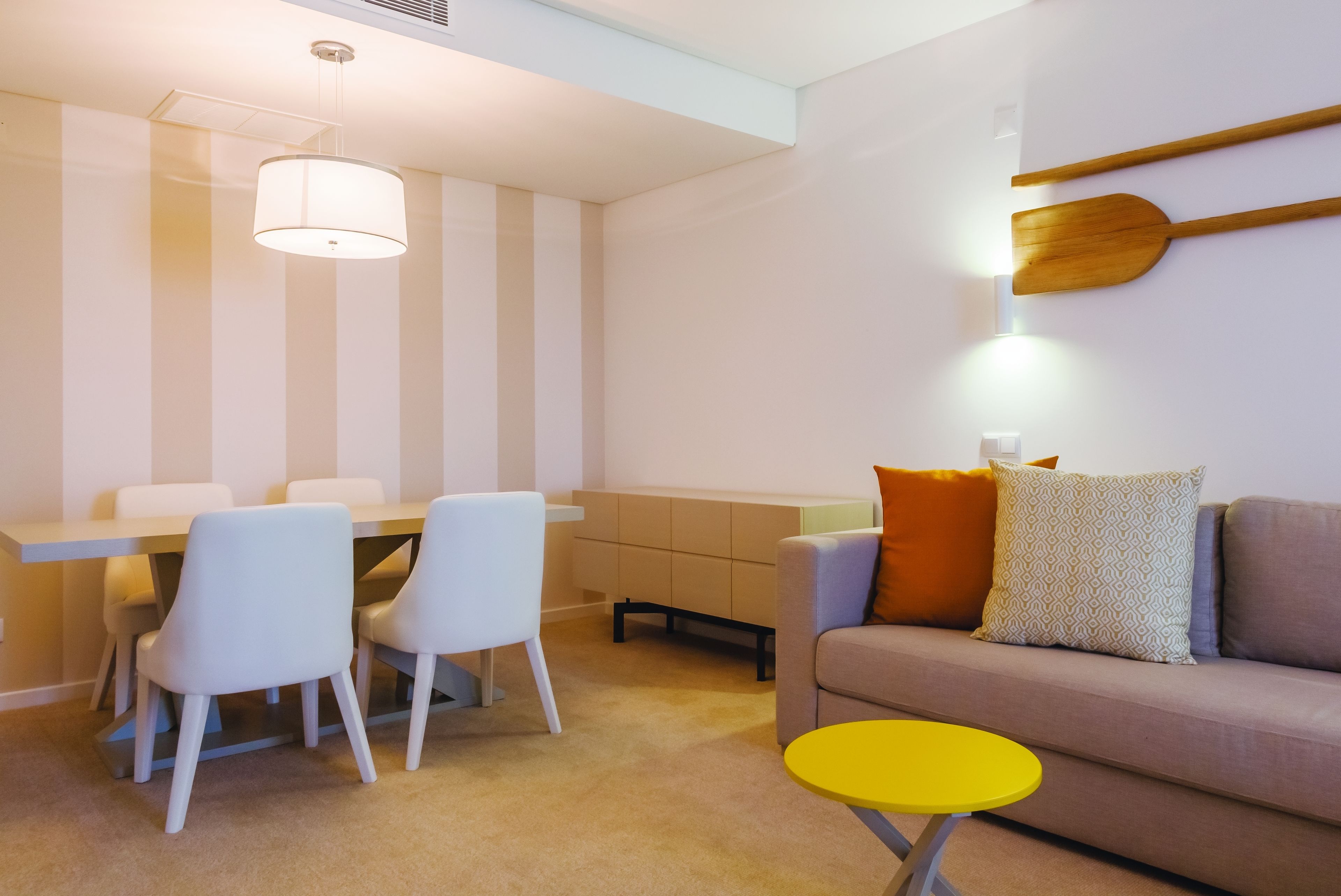 Una sala de estar moderna con comedor, que incluye un sofá, sillas, una mesita amarilla y una espátula de madera colgante.