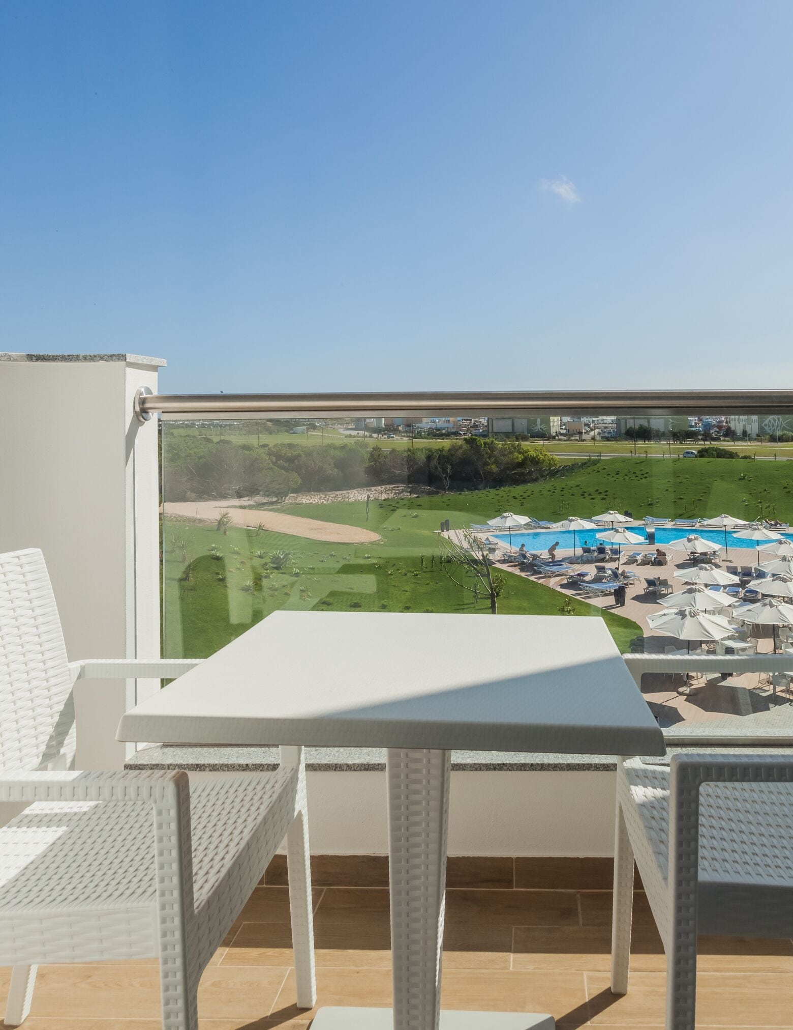 A balcony with a view of a pool area, including lounge chairs and umbrellas.