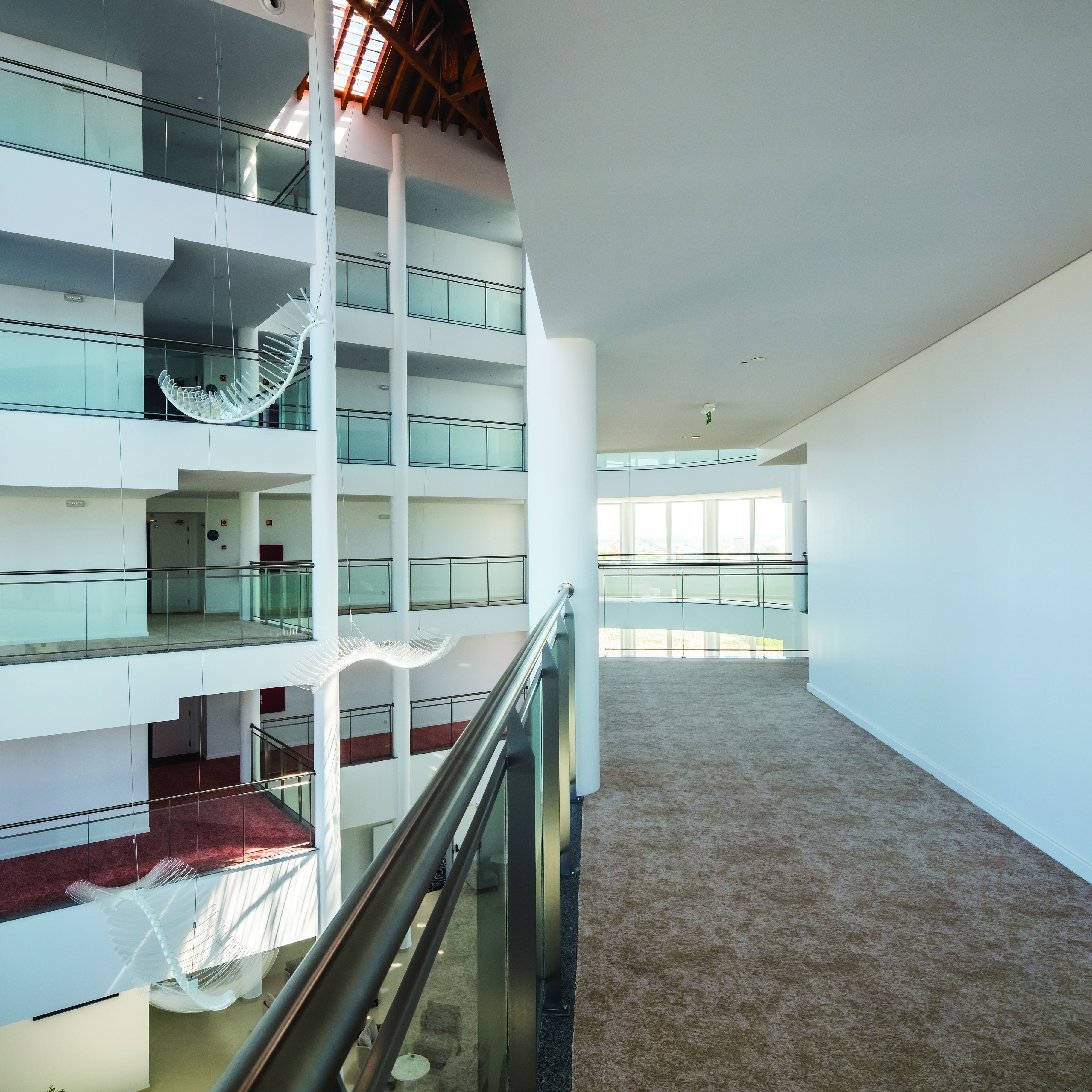 Un intérieur à plusieurs niveaux, doté de rampes en verre, d’un escalier central en colimaçon et d’un plancher recouvert de moquette.
