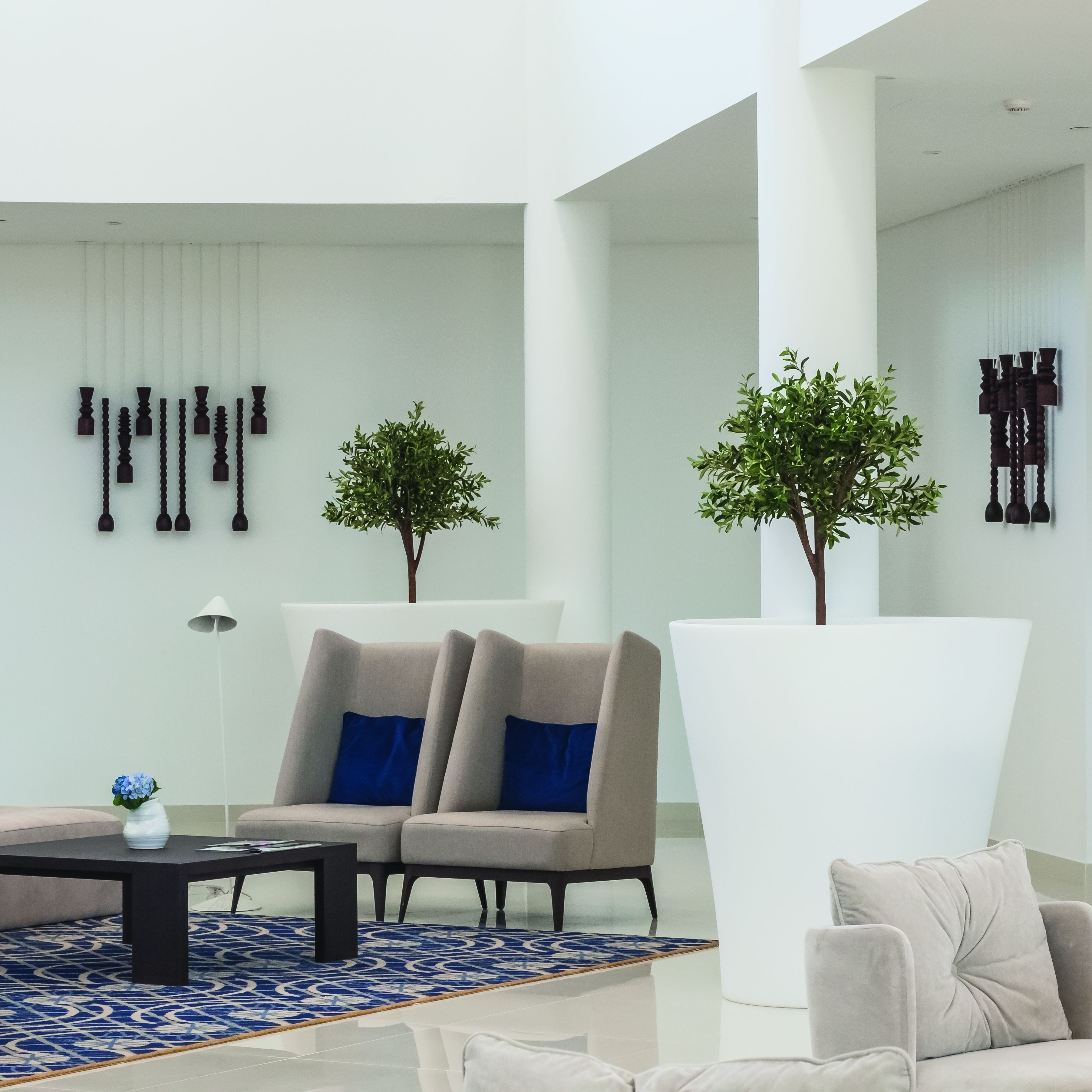 Uma sala de estar moderna com dois sofás, uma mesa de centro e elementos decorativos como esculturas na parede e plantas em vasos.