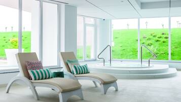 Relax in a serene space with a hot tub, lounge chairs, and a large window offering a view of the well-maintained lawn.
