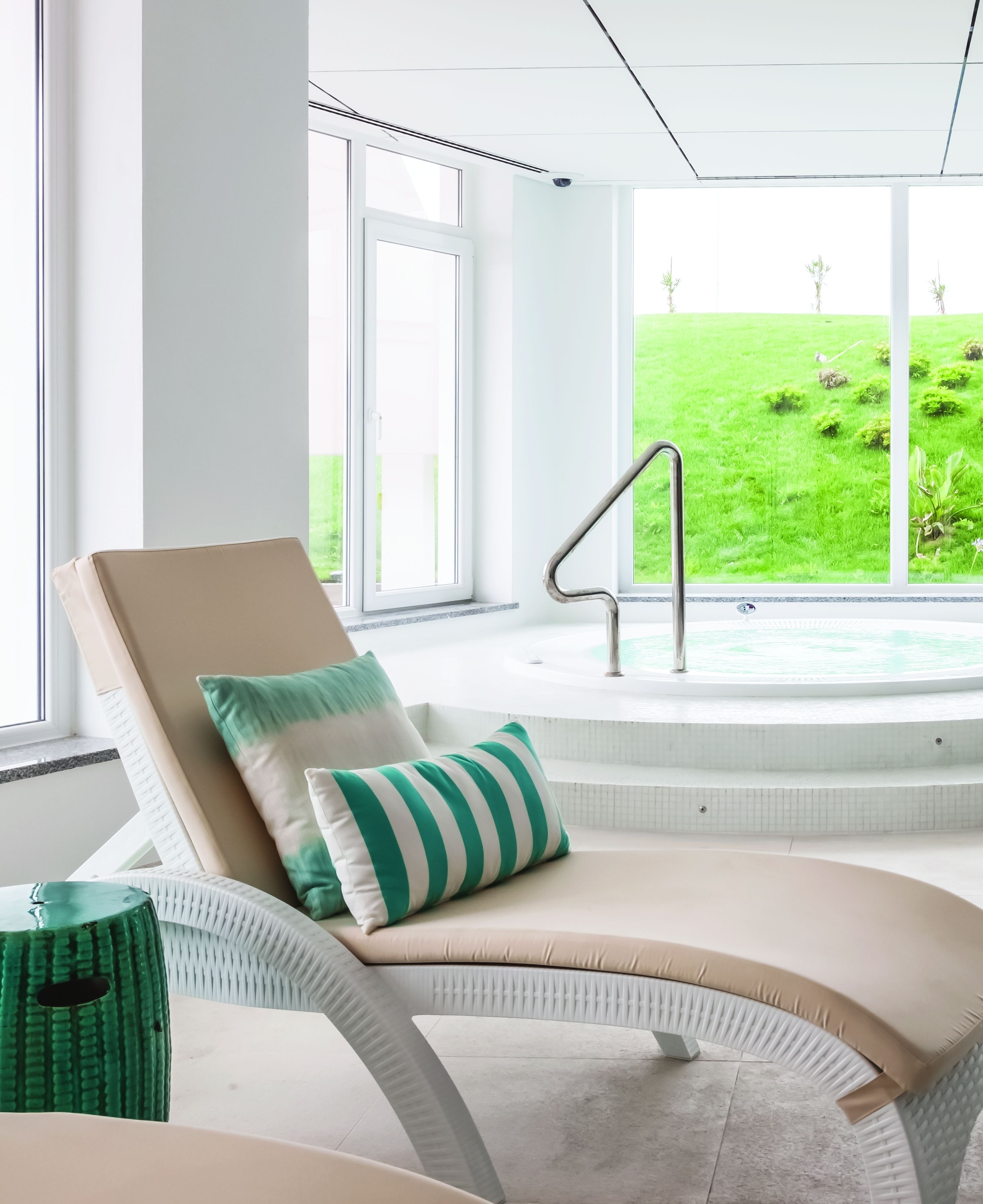 A modern lounge area with a reclining chair, a green and white striped pillow, and a view of a green lawn through large windows.