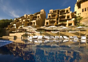 Un hôtel doté d’un espace piscine comprenant des chaises longues et des parasols, le tout entouré d’immeubles à plusieurs étages présentant un style architectural unique.
