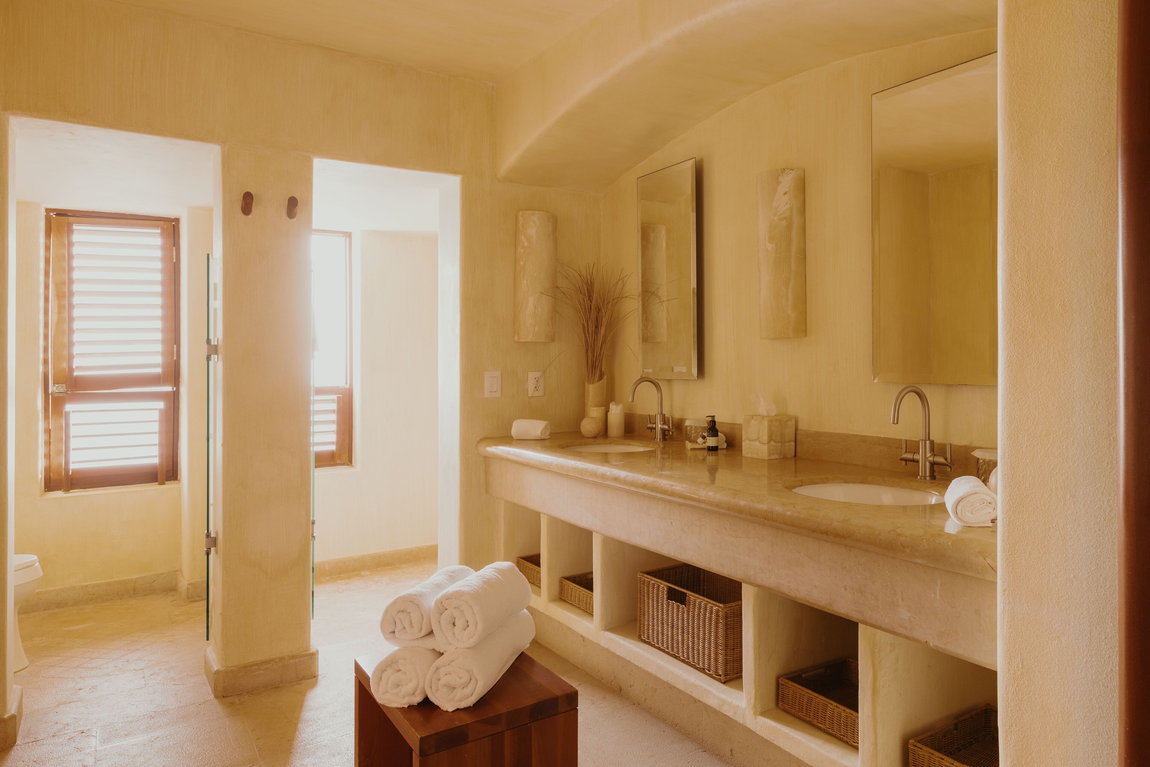 Un baño con un lavamanos grande, un espejo y dos cestos debajo del mueble.
