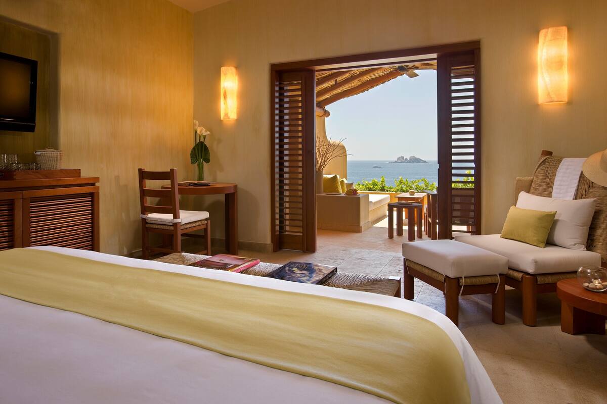 Een hotelkamer met een bed, bureau, stoel, bank en uitzicht op zee.