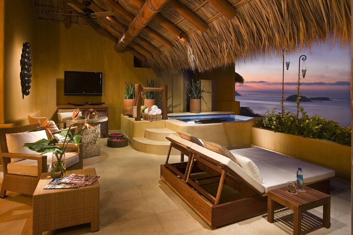 Een luxueuze buitenzitplaats met een rieten dak, een jacuzzi en een televisie.