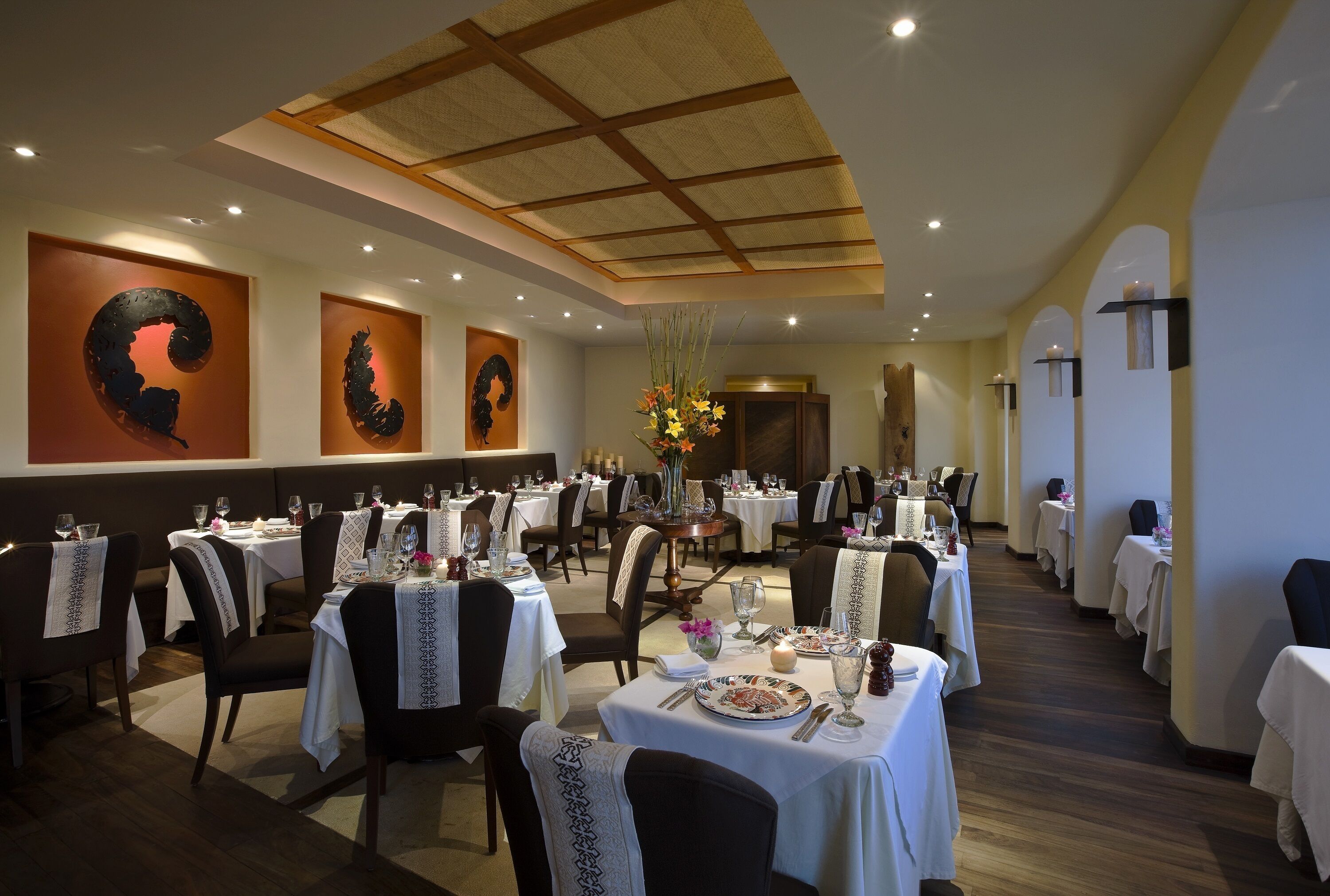Un restaurante con varias mesas dispuestas para comer, con una decoración moderna que incluye un techo alto y arte decorativo en las paredes.