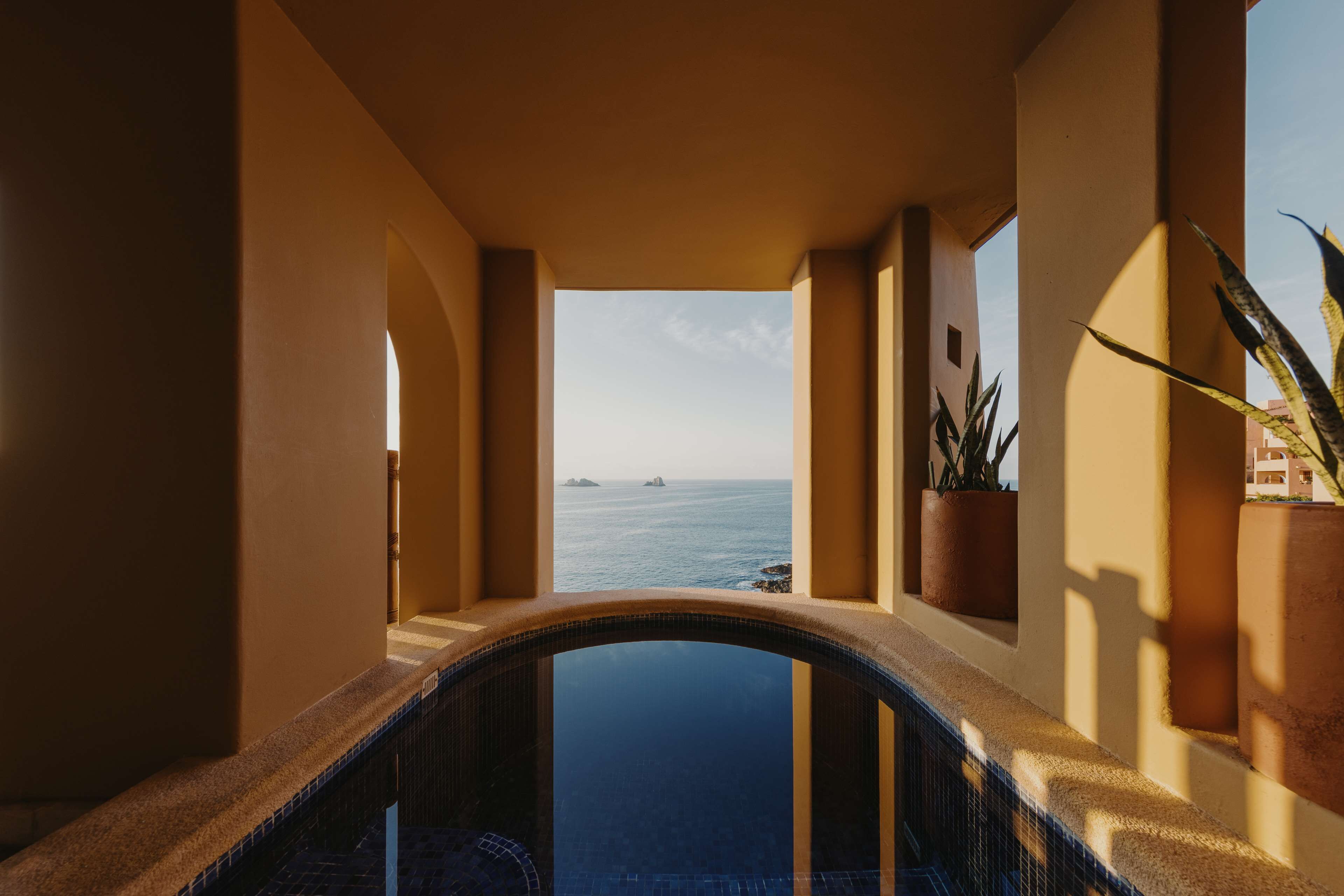 A pool area with a view of the sea, a tiled floor, and potted plants.
