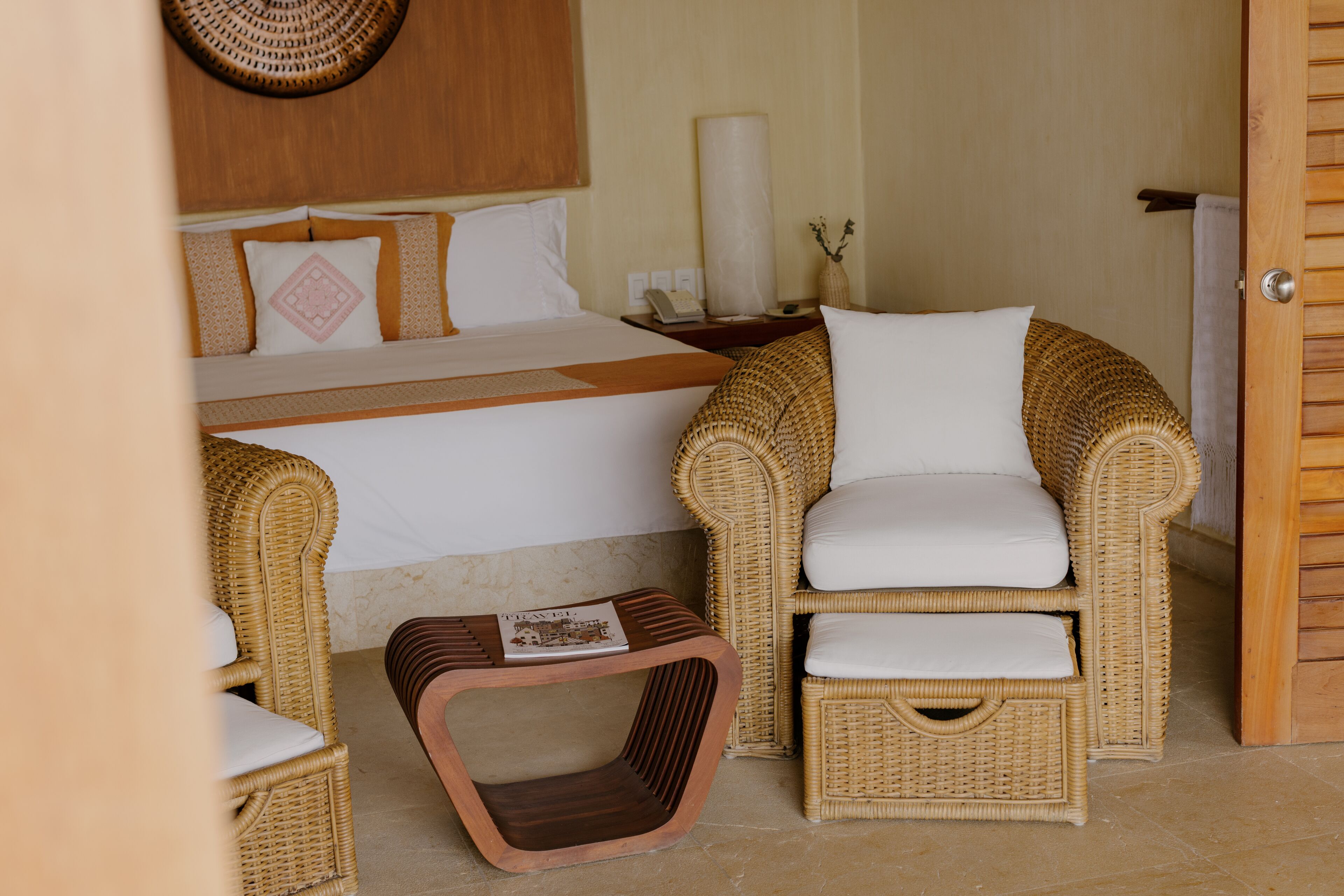 Ein Hotelzimmer mit einem Bett, zwei Korbstühlen, einem kleinen Holztisch und einem Wandbild.