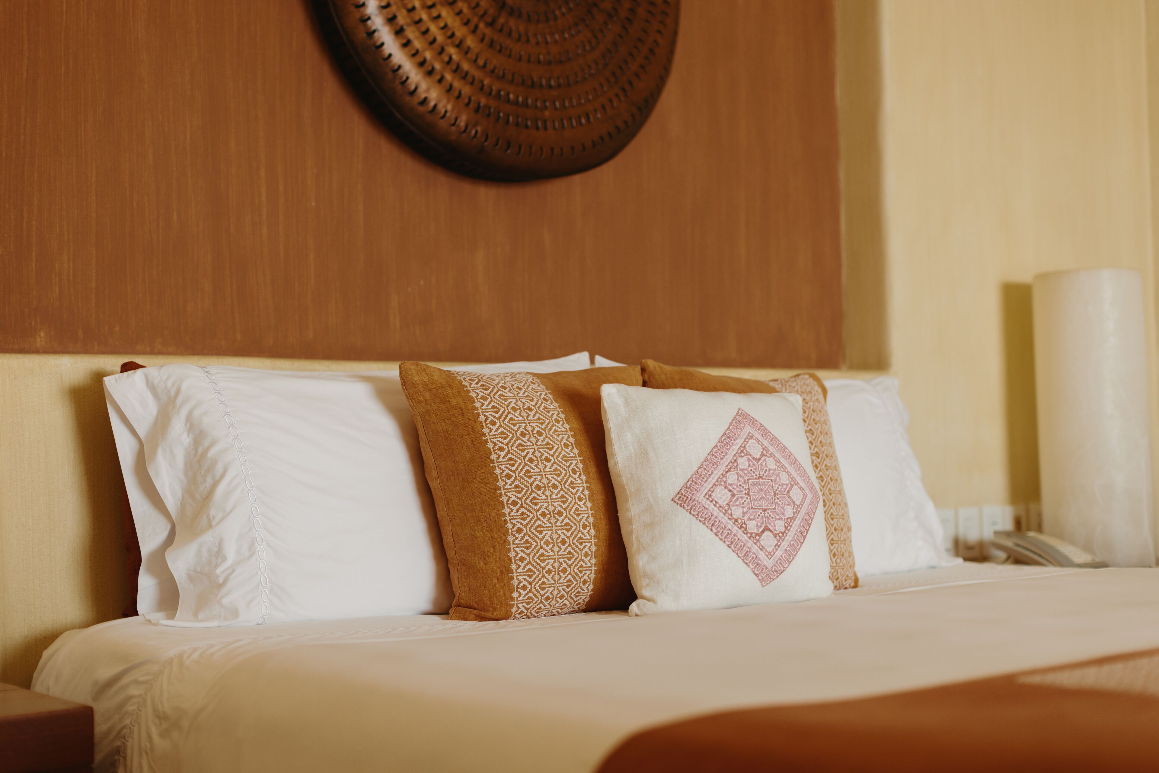 A neatly made bed with white and patterned pillows, a wooden headboard, and a wall-mounted decorative item.