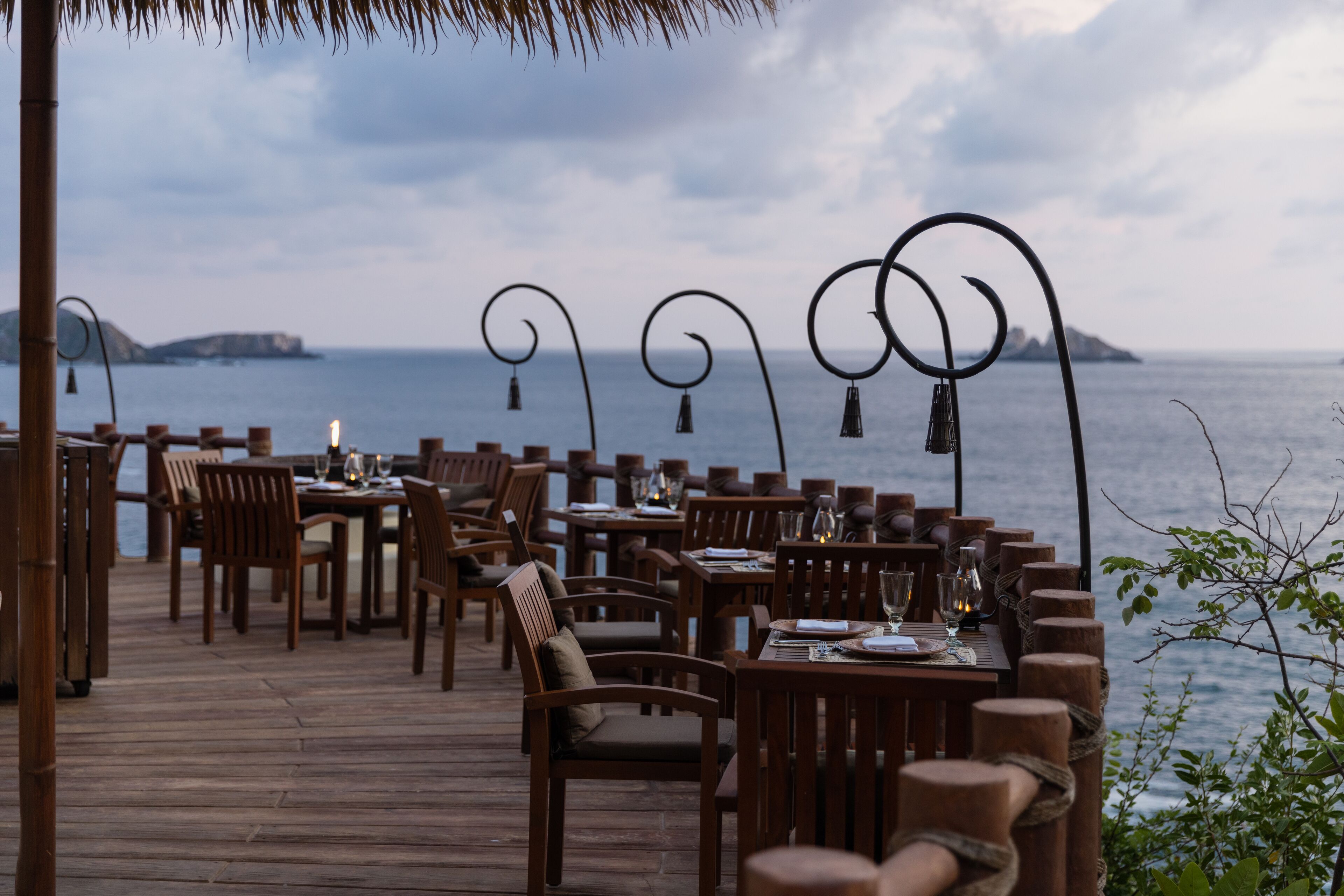 A wooden deck with tables and chairs, overlooking a body of water with islands in the distance.