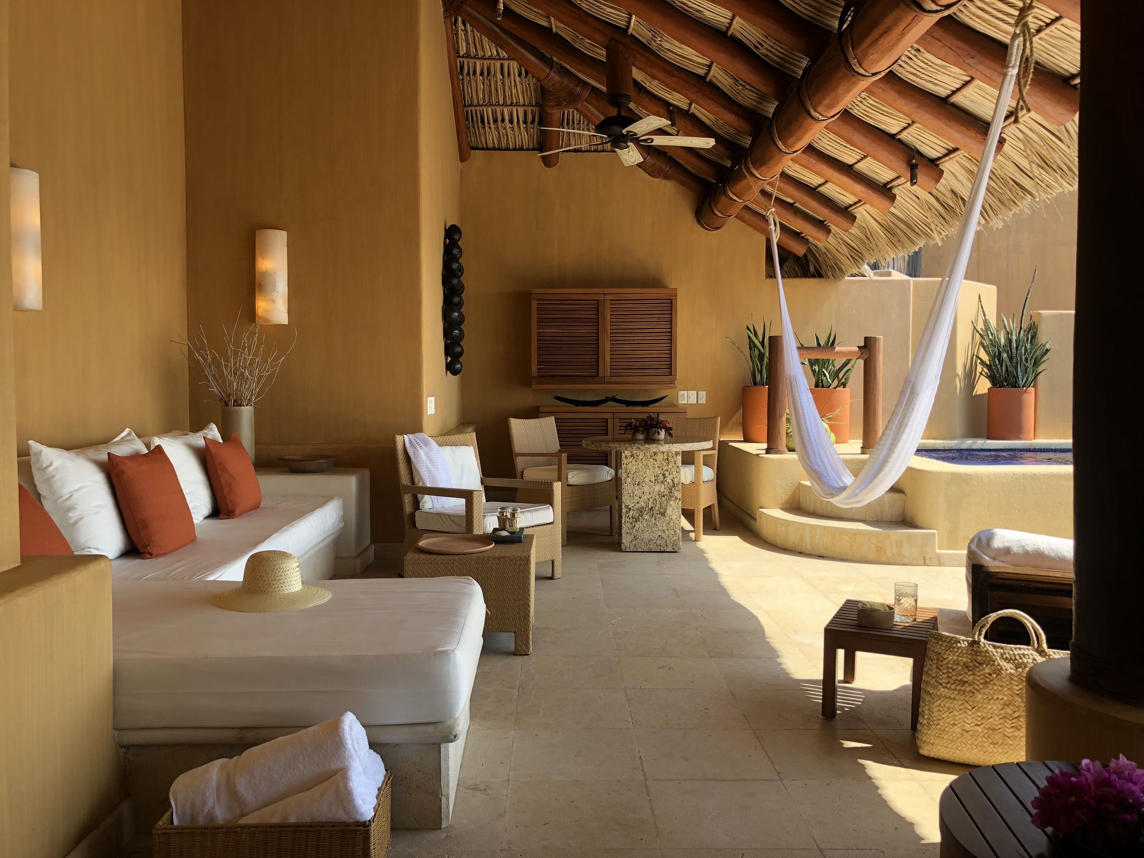 A spacious outdoor lounge area with a thatched roof, comfortable seating, and a small pool.