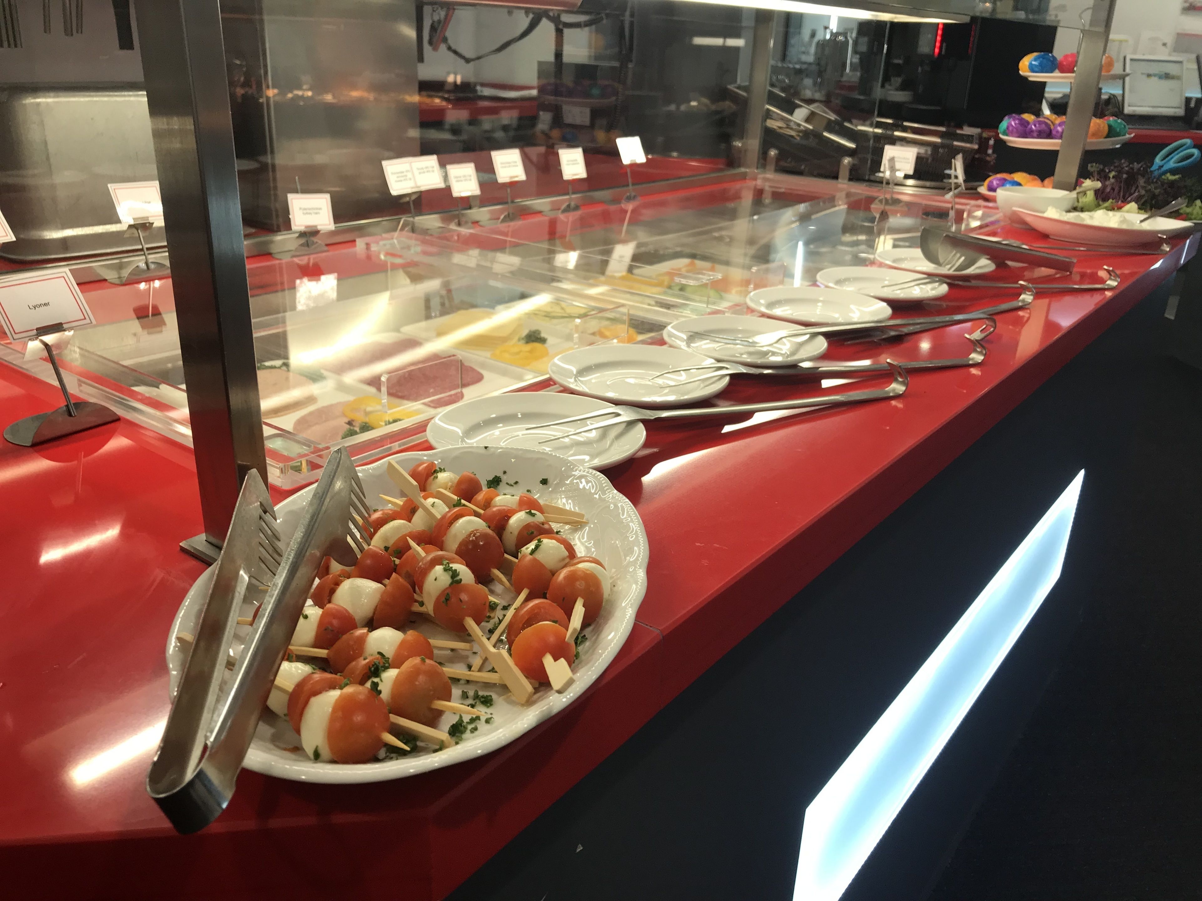 Ein Buffetbereich mit verschiedenen Speisen, die in einer Glassäule präsentiert werden, darunter Spieße aus Tomaten und Mozzarella.