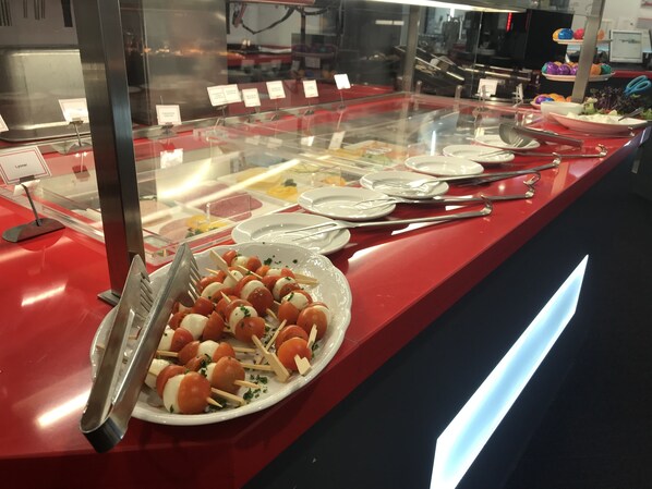 Zona de bufé con diversos platos expuestos en una vitrina, incluyendo brochetas de tomate y mozzarella.