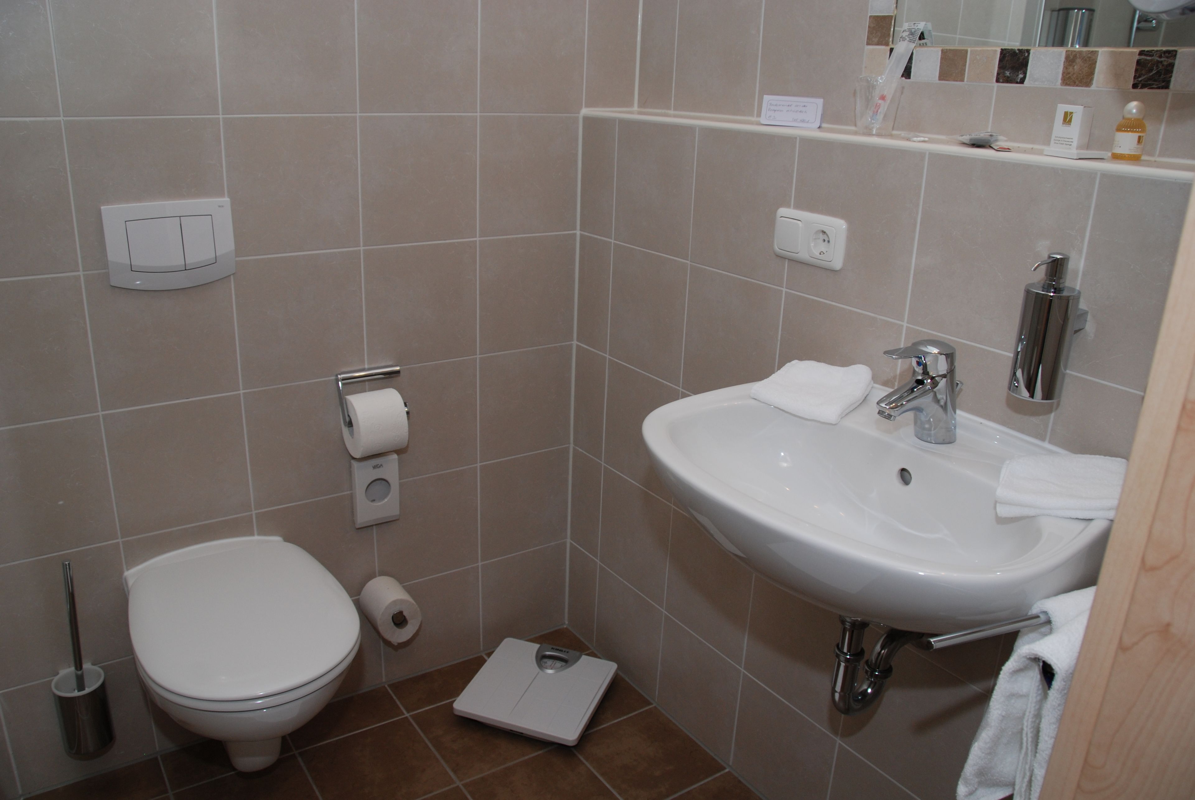 A bathroom with a toilet, sink, and a weighing scale on the floor.