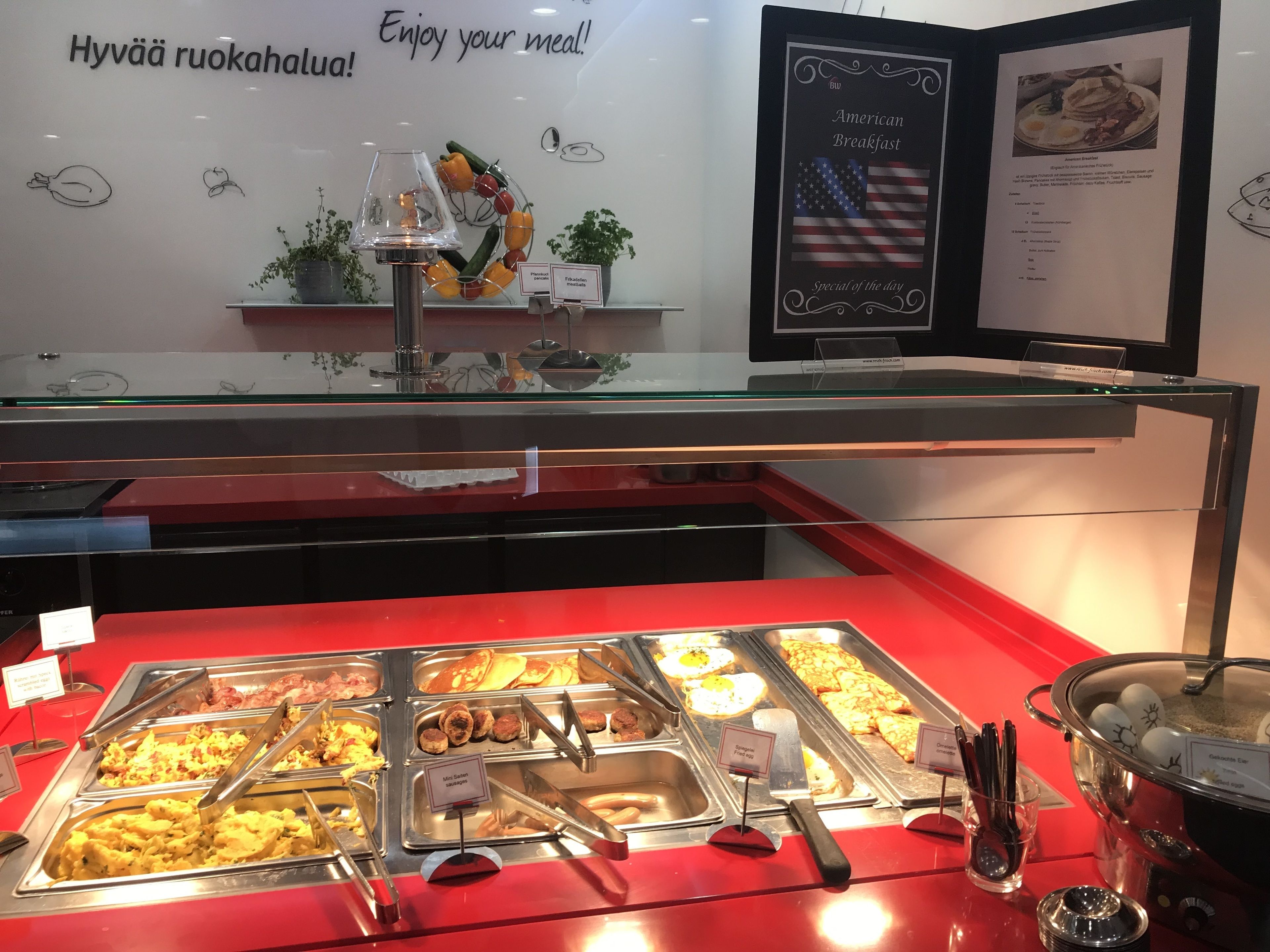 A buffet area with various food options, a menu board, and a wall with a motivational message.