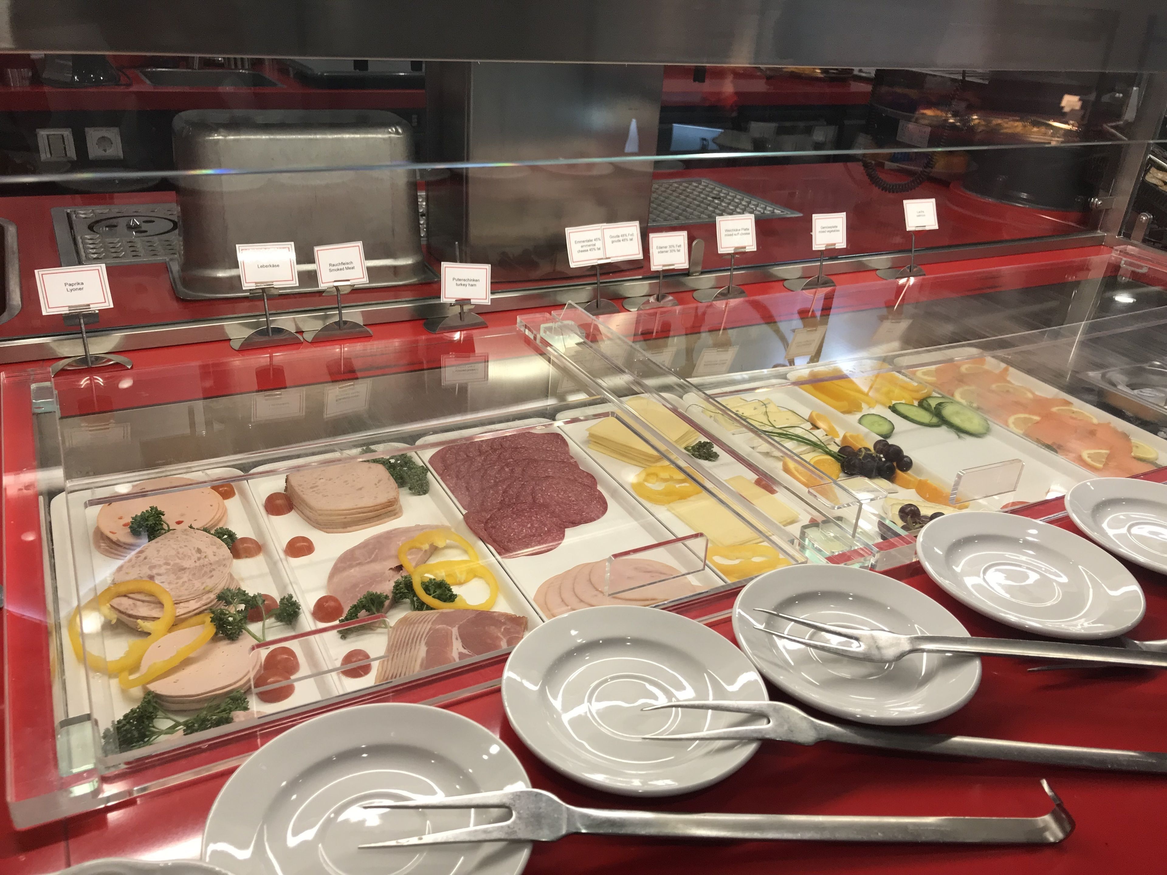 A deli counter with various meat and cheese options, plates, and utensils.