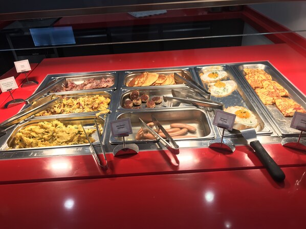 Un bufé con diversas opciones de comida, incluyendo huevos revueltos, salchichas y tortillas.