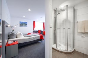 Una habitación de hotel moderna con cama, mesita de noche y zona de ducha.