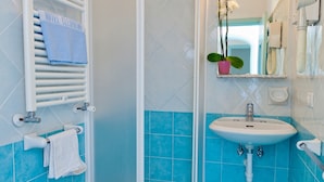 A bathroom with a white sink, a shower, and a towel rack with a blue towel. - Hotel Cleopatra (Ischia)