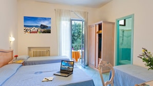 A hotel room with two beds, a laptop on one bed, a view of the sea through the window, and a balcony with a table and chairs. - Hotel Cleopatra (Ischia)