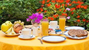 A table set with breakfast items including fruits, bread, and beverages, surrounded by lush greenery and vibrant flowers. - Hotel Cleopatra (Ischia)