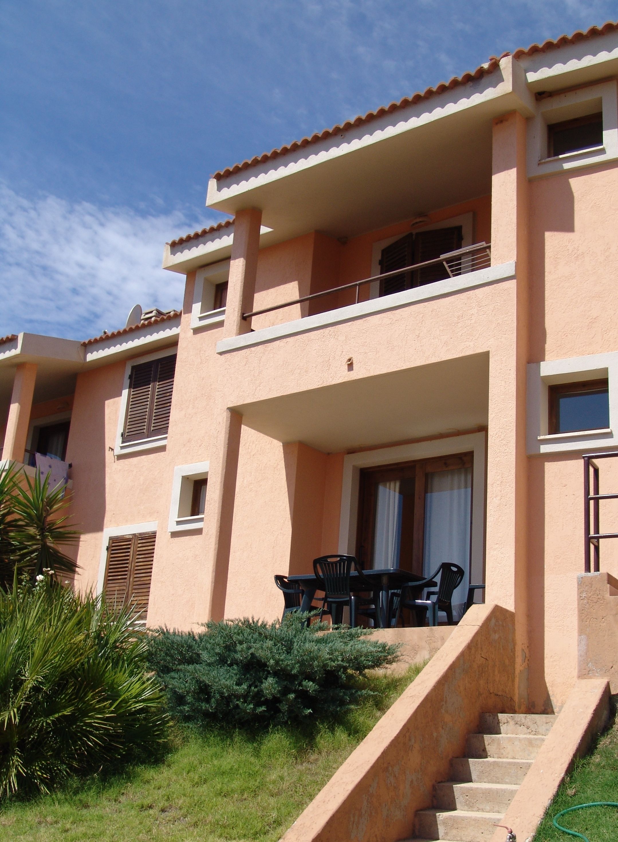 A multi-story building with a balcony, outdoor seating, and a staircase leading to the entrance.