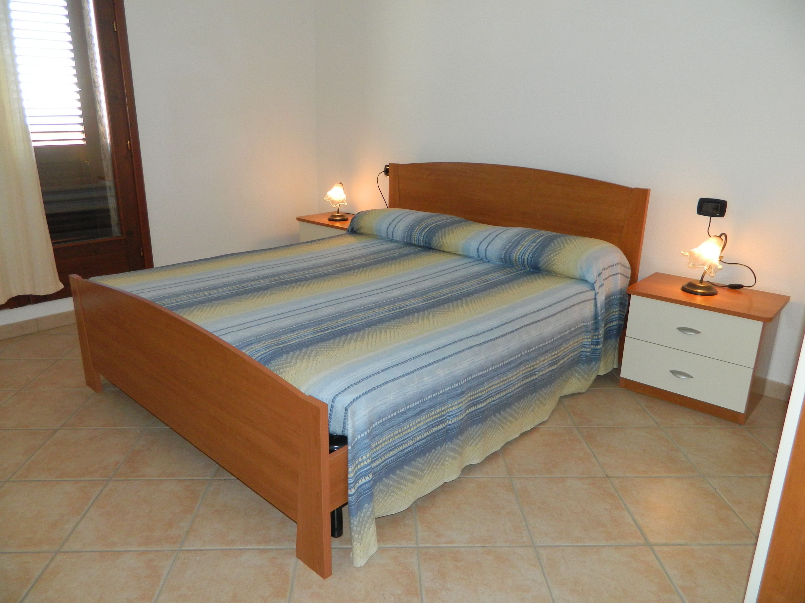 Une chambre à coucher avec un lit en bois, une literie à rayures, une table de chevet avec une lampe et un tiroir.