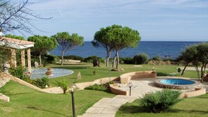 A landscaped outdoor area with a pool, stone pathways, and a view of the sea. - Villaggio Porto Corallo (Villaputzu)
