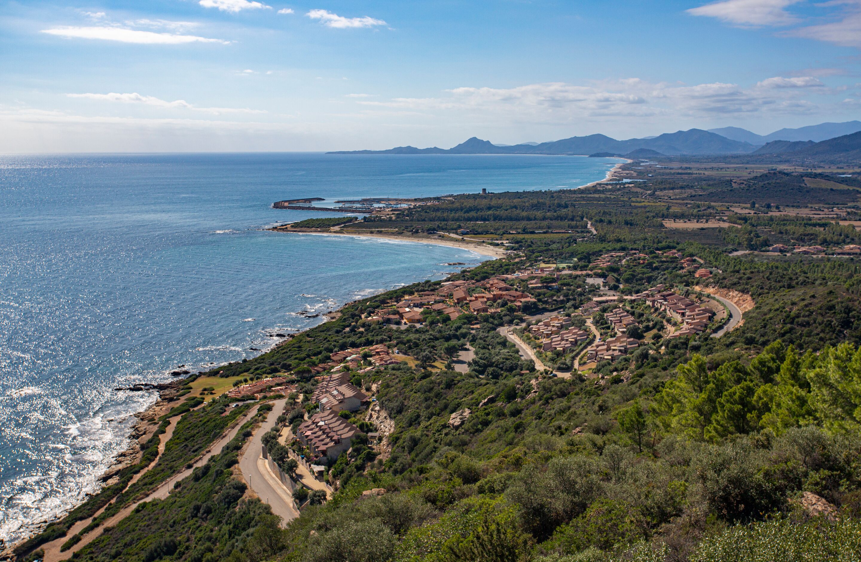 A coastal town with terraced houses, a beach, and mountains in the distance.
