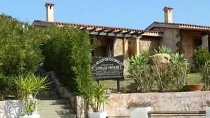 A villa with a stone facade, terracotta roof tiles, and a sign indicating it is a vacation rental. - Villaggio Porto Corallo (Villaputzu)