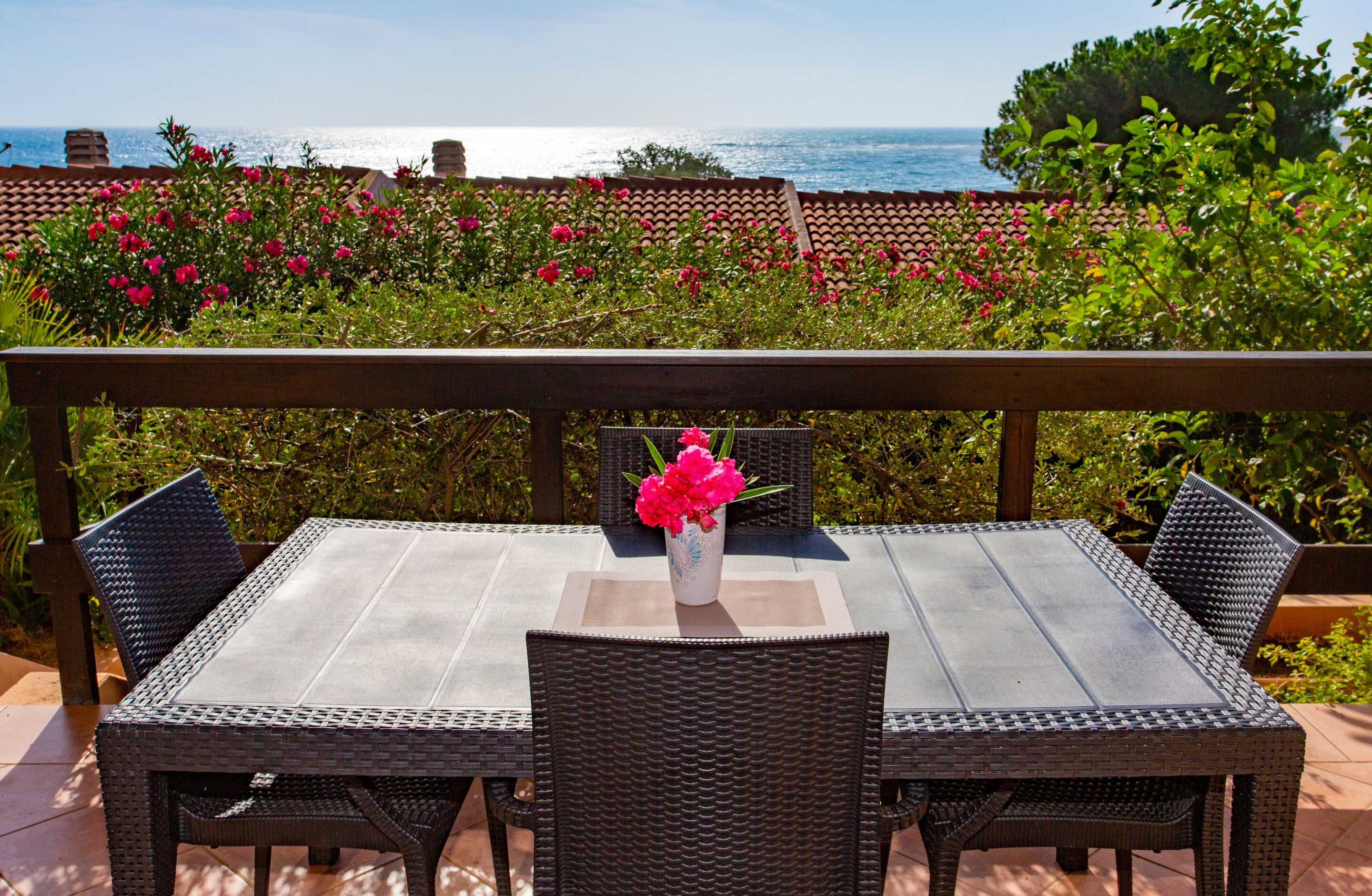 An outdoor patio with a table and chairs, a vase of flowers, and a view of the sea.