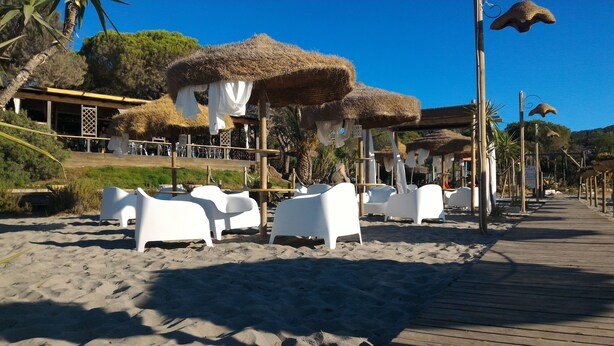 A beachside area with thatched umbrellas, white lounge chairs, and a wooden boardwalk. - Villaggio Porto Corallo (Villaputzu)