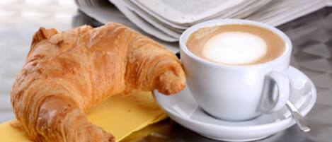 Et croissanter og en kop kaffe på et glastop med aviser.