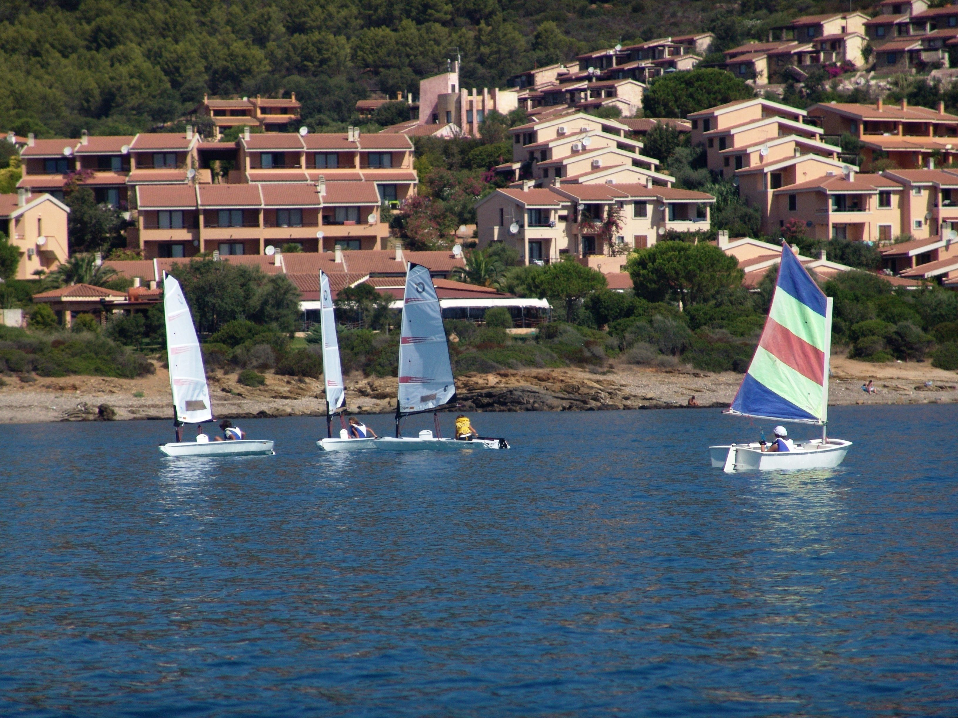 A coastal town with multiple-story buildings, some with balconies, and sailboats on the water.