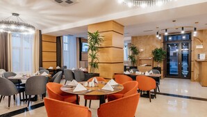 A modern hotel dining area with round tables, orange and gray chairs, and a central wooden pillar. - Ramada by Wyndham Astana (Astana)