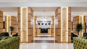 A modern hotel lobby with a central reception desk, wooden paneling, and green upholstered sofas. - Ramada by Wyndham Astana (Astana)