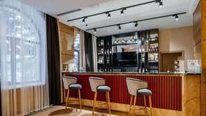 A bar area with three bar stools, a television, and shelves stocked with bottles. - Ramada by Wyndham Astana (Astana)