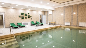 En swimmingpool med ett kaklat botten och en klar vattenyta. Längs poolkanten står gröna solstolar.