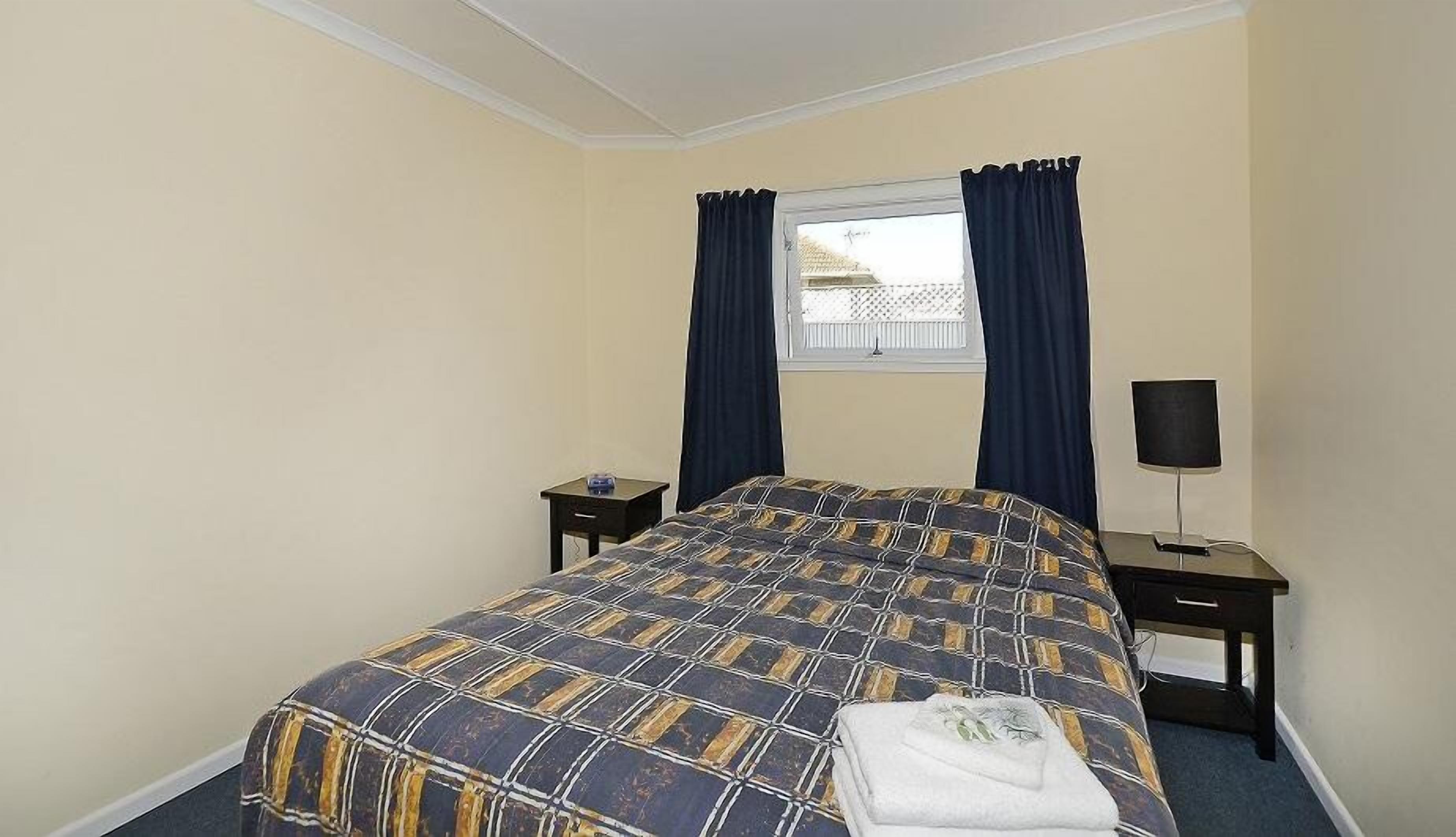 A bedroom with a bed, a nightstand, a lamp, and a window with curtains.