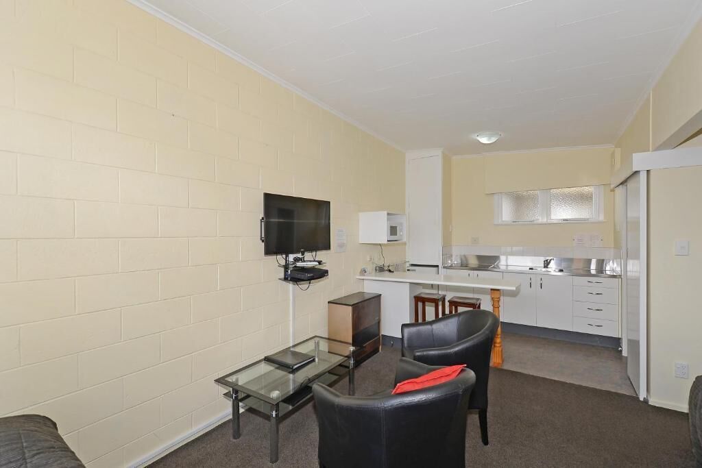 Un espacio habitable compacto con kitchenette, un televisor de pantalla plana montado en la pared y una mesa de centro de vidrio.