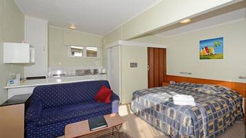 A compact hotel room with a kitchenette, a sofa, a bed, and a small table.