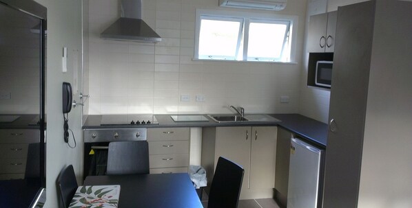 Cocina compacta con estufa, pileta y microondas. Hay una ventana que proporciona luz natural y una silla en la mesa.
