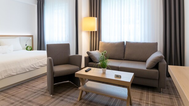 Ein Hotelzimmer mit Bett, Sofa, Couchtisch und Lampe.