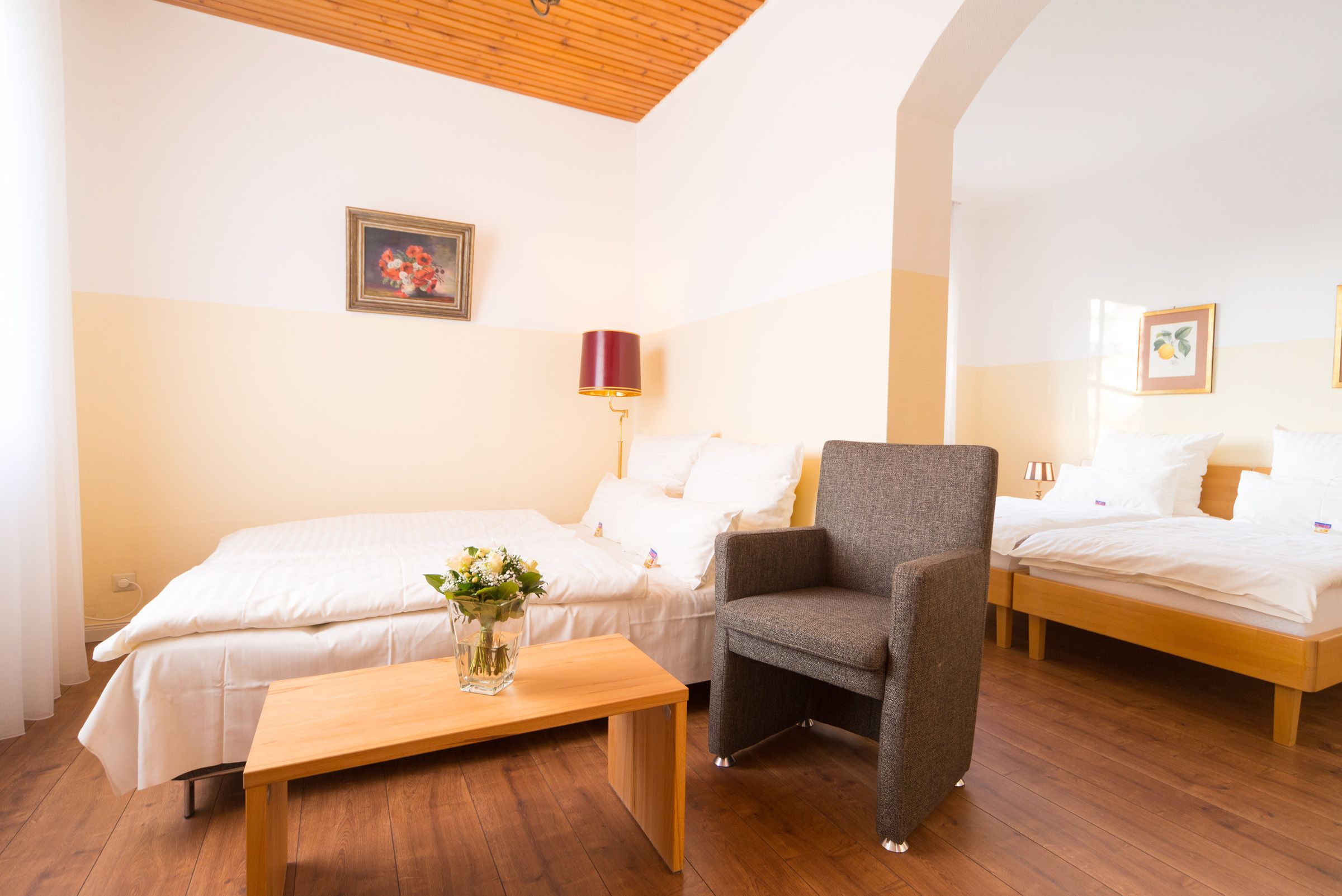 Una habitación con dos camas, una mesa de madera, una silla y una lámpara.