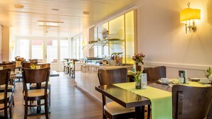 Ein geräumiges Restaurant mit Holztischen und -stühlen, einer Küche im Hintergrund und freundlicher, heller Atmosphäre.