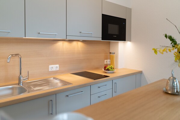 A modern kitchen with a stainless steel sink, a black microwave, and a wooden countertop.