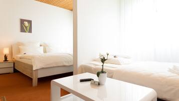 A hotel room with two beds, a bedside table with a remote control, a potted plant, and a name tag on the table.