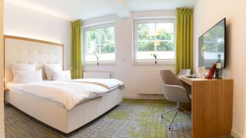 Quarto de hotel com cama, escrivaninha, cadeira, espelho grande e duas janelas com cortinas.